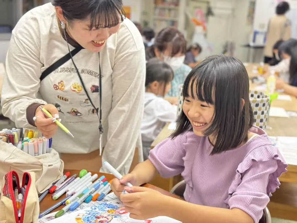 講師と一緒に色鉛筆の作品を仕上げる子どもの受講生